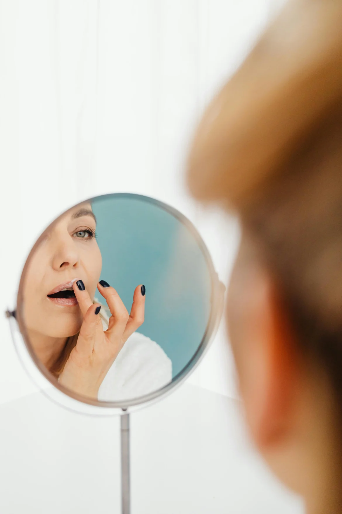 A woman applying a lip sleeping mask while looking into a round mirror, close-up of moisturized lips and gentle application.